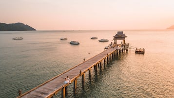 A wooden pier extending into calm waters with boats and a traditional structure at the end.