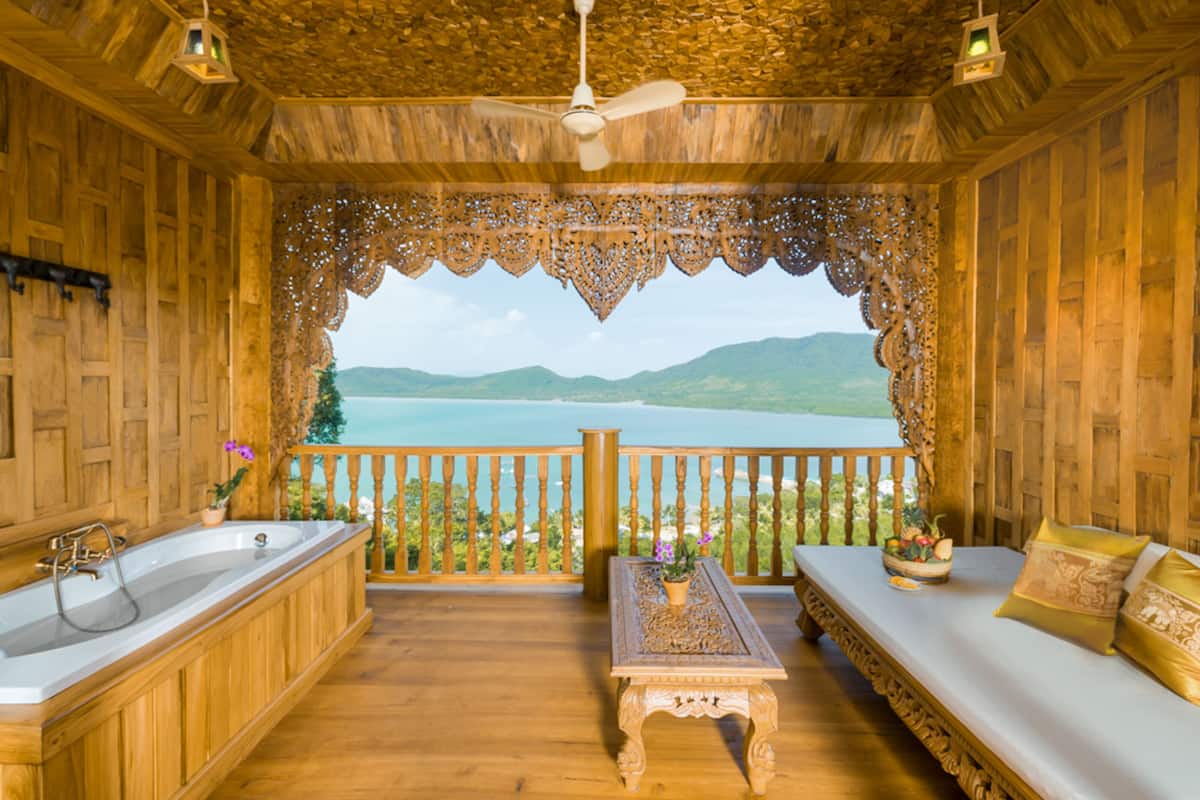 A wooden room with a bathtub, a table with a flower vase, and a sofa with cushions.