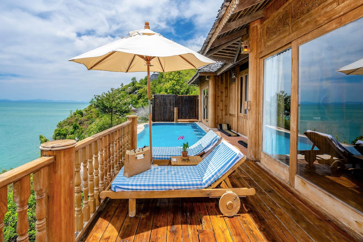 A wooden deck with a pool, lounge chairs, and an umbrella.