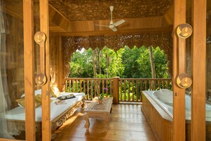 Una terraza de madera con una cama, una mesa con un jarrón y un jacuzzi.
