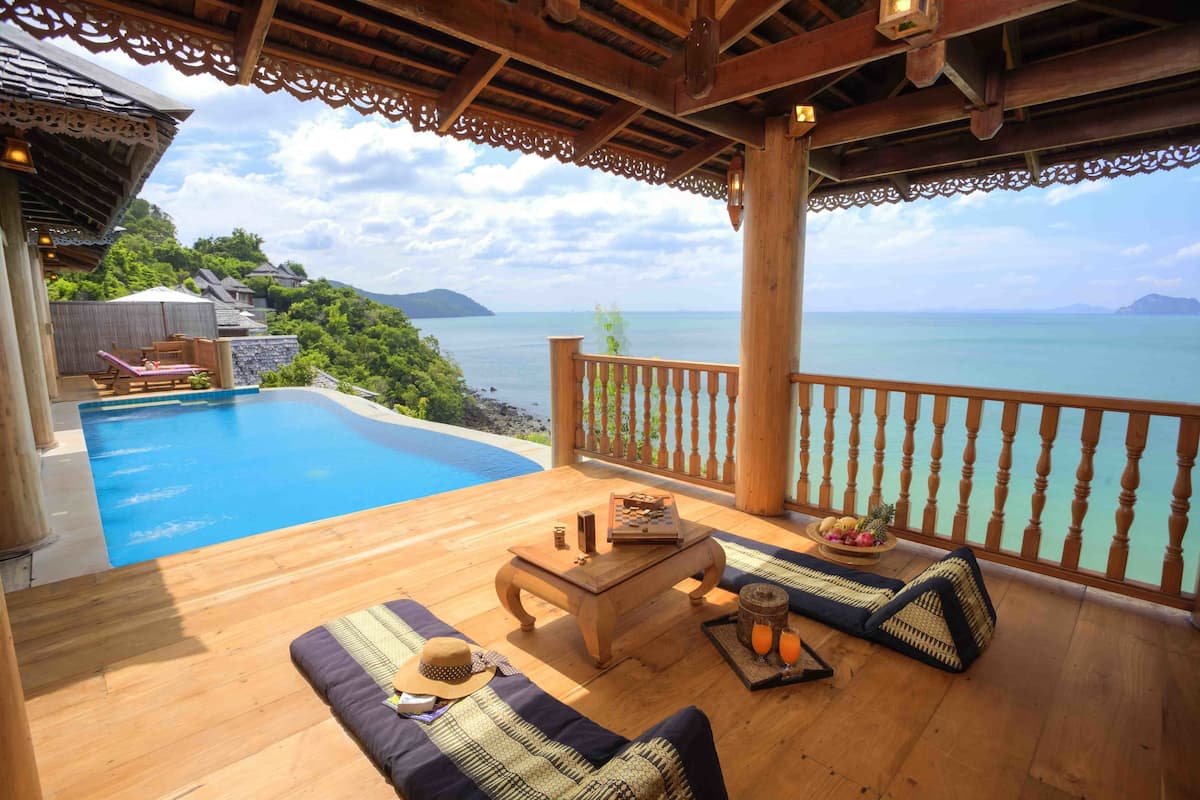 A wooden deck with a pool, lounge chairs, and a table with drinks and snacks.