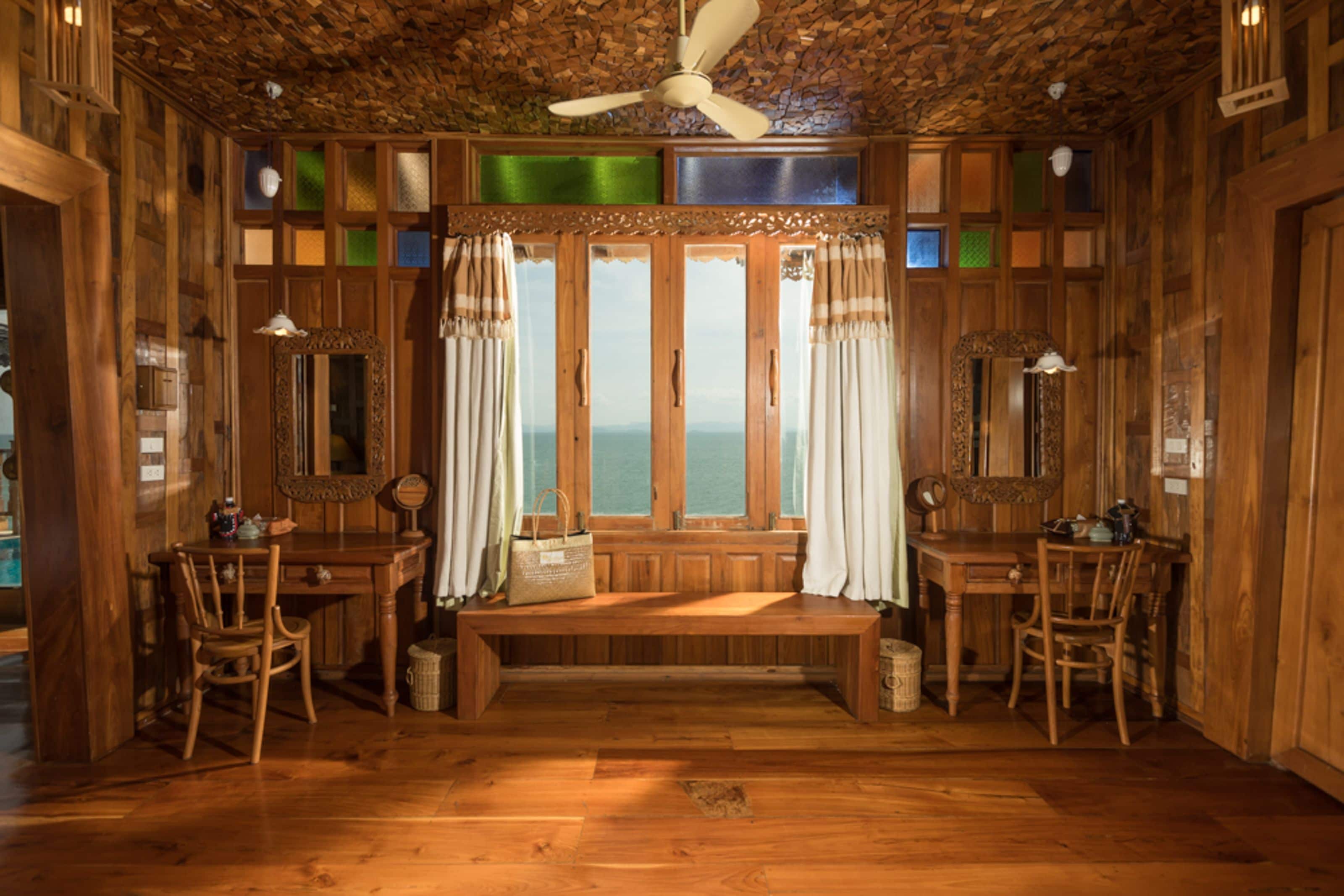 A wooden room with a large window, a ceiling fan, and two wooden tables with chairs.