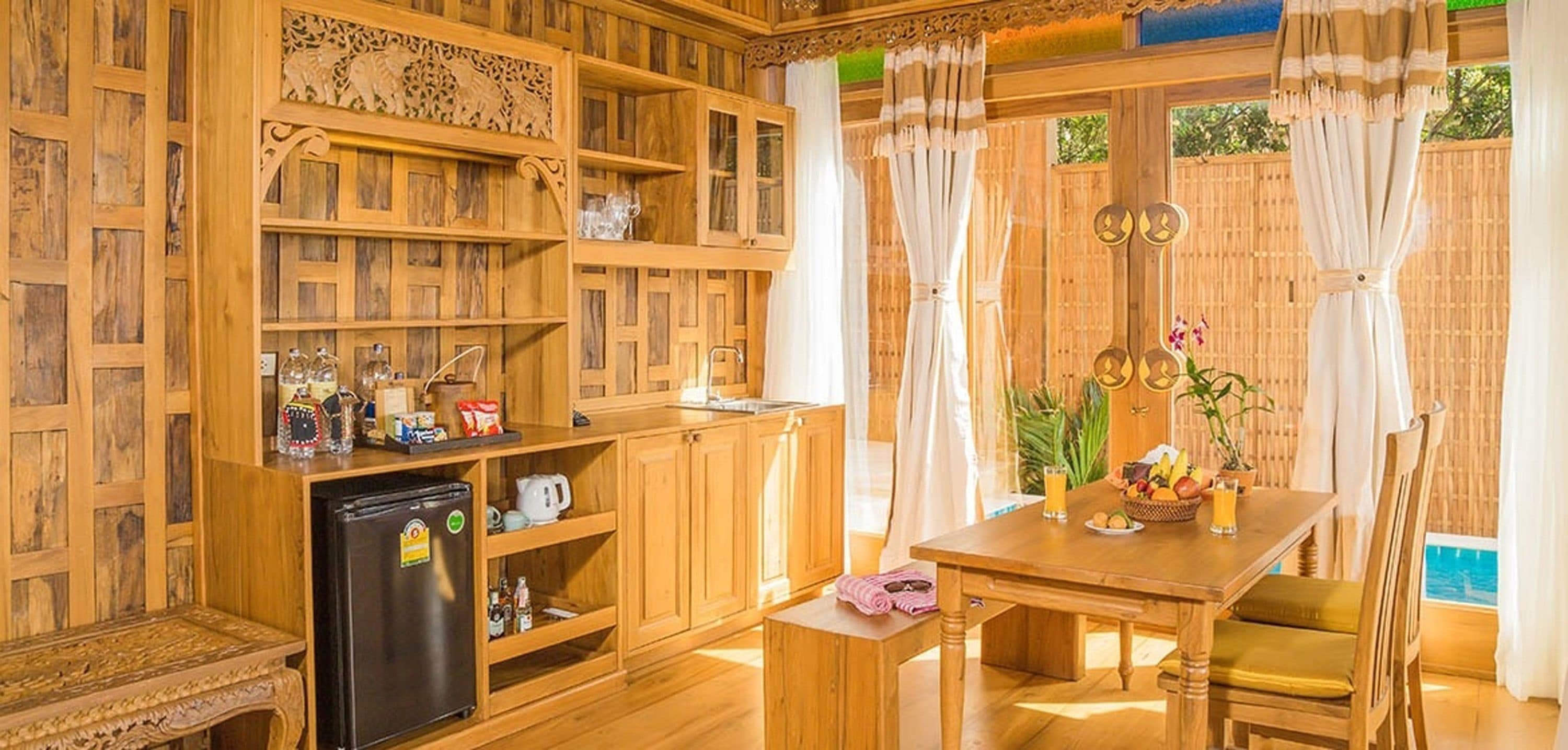 Un interior de madera con una mesa de comedor, sillas, un refrigerador y estantes con diversos objetos.