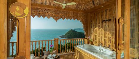 A wooden spa room with a large bathtub, a ceiling fan, and a view of the sea.