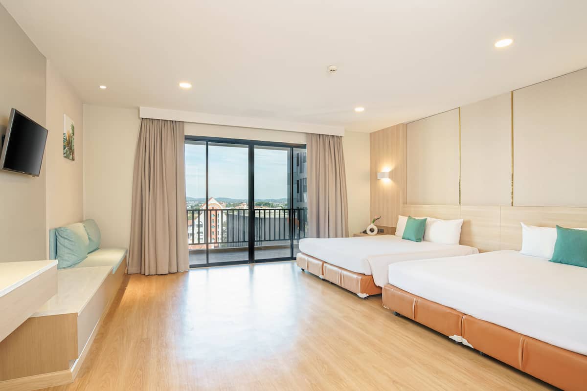 A hotel room with two beds, a desk, a TV, and a balcony with a view of the city.