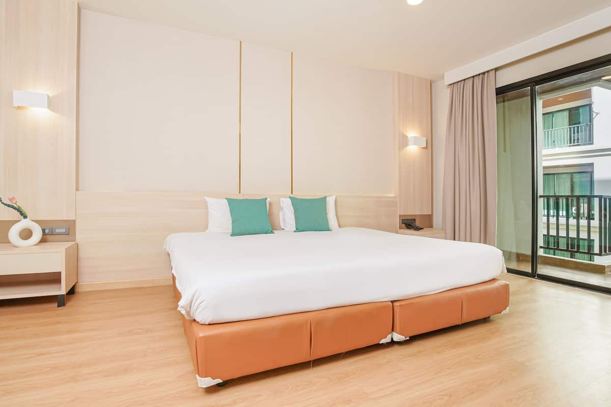 A modern hotel room with a large bed, wooden flooring, and a view of a balcony.