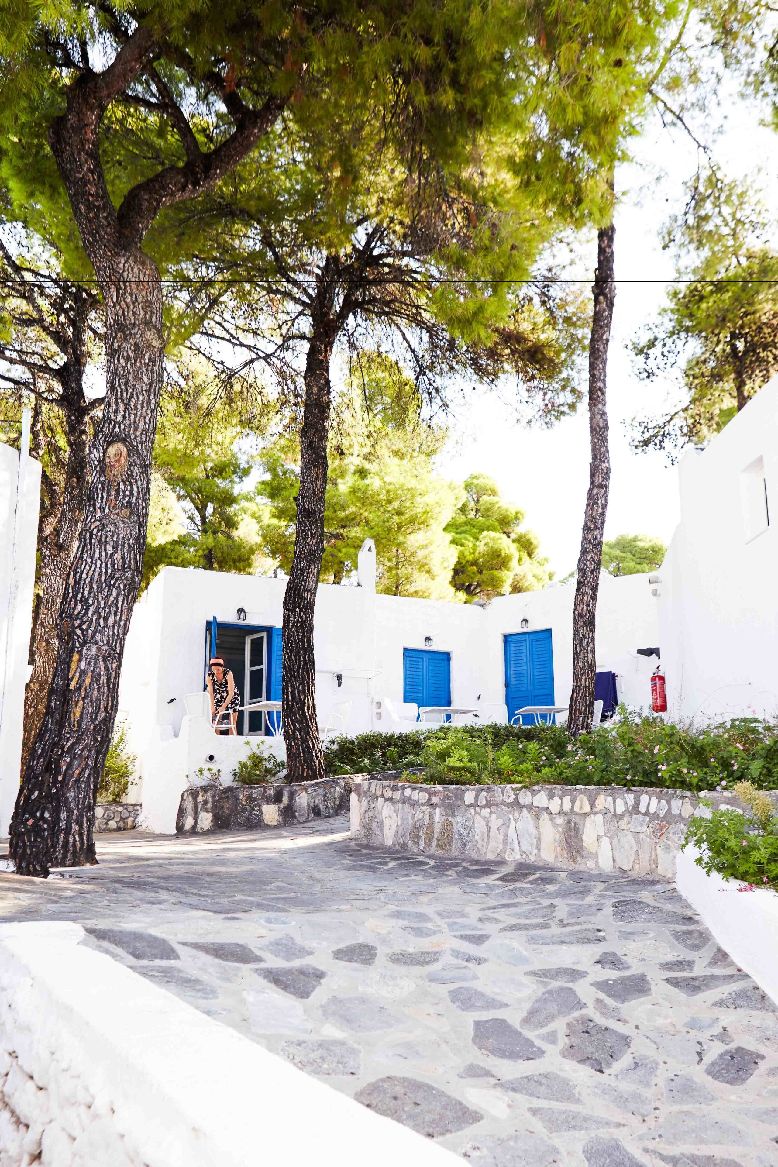 A white building with blue shutters, a stone pathway, and trees.