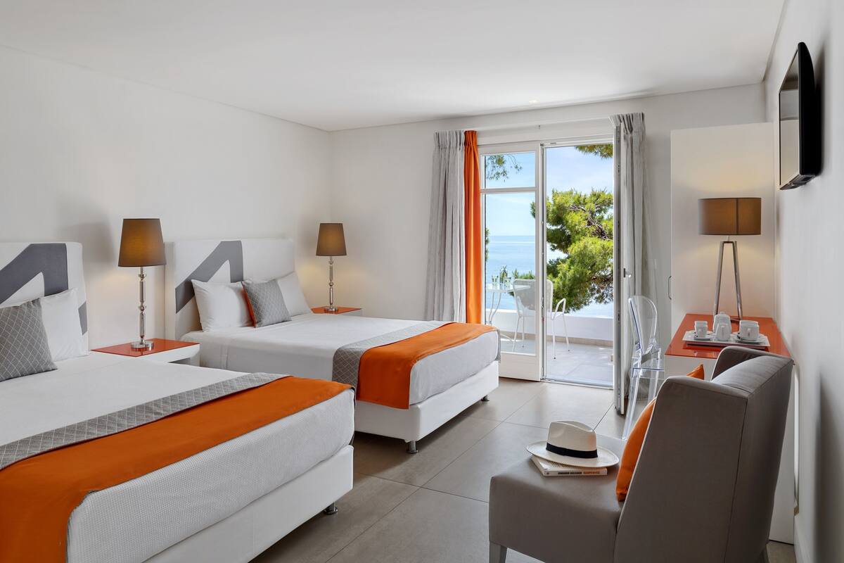 A hotel room with two beds, a seating area, and a balcony with a view.