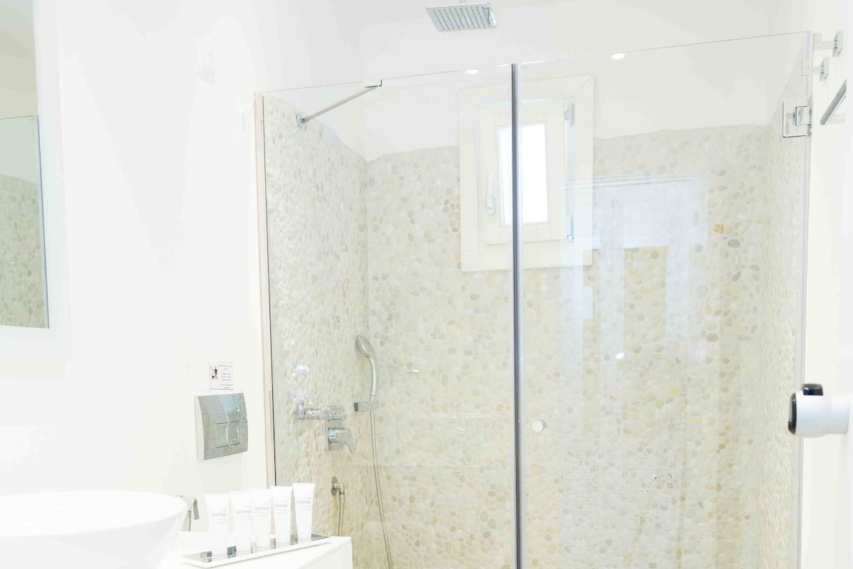 Un baño moderno con ducha envuelta en vidrio, un lavamanos blanco y un espejo grande.
