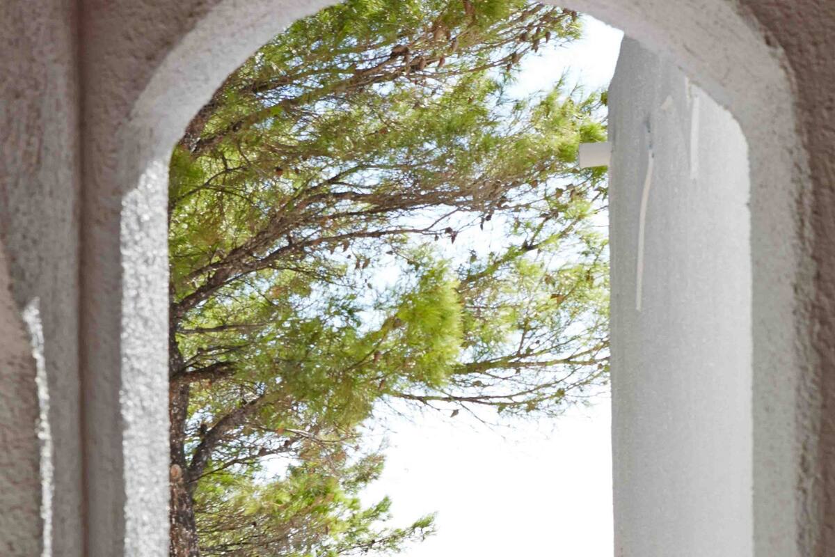 An arched doorway leading to a balcony with a view of the sea and trees.