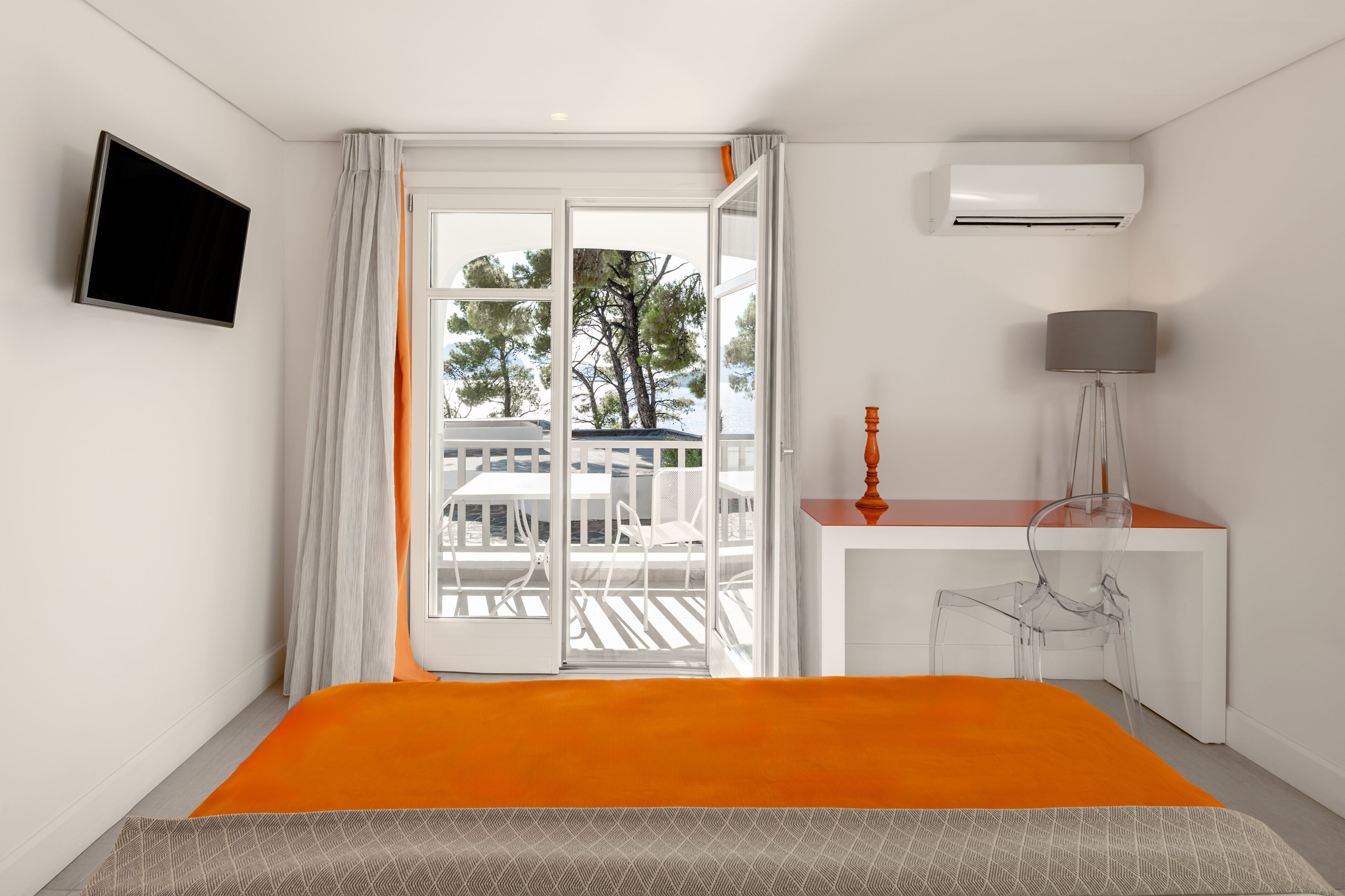 A hotel room with a bed, a desk, a chair, a TV, and a view of the outdoors.