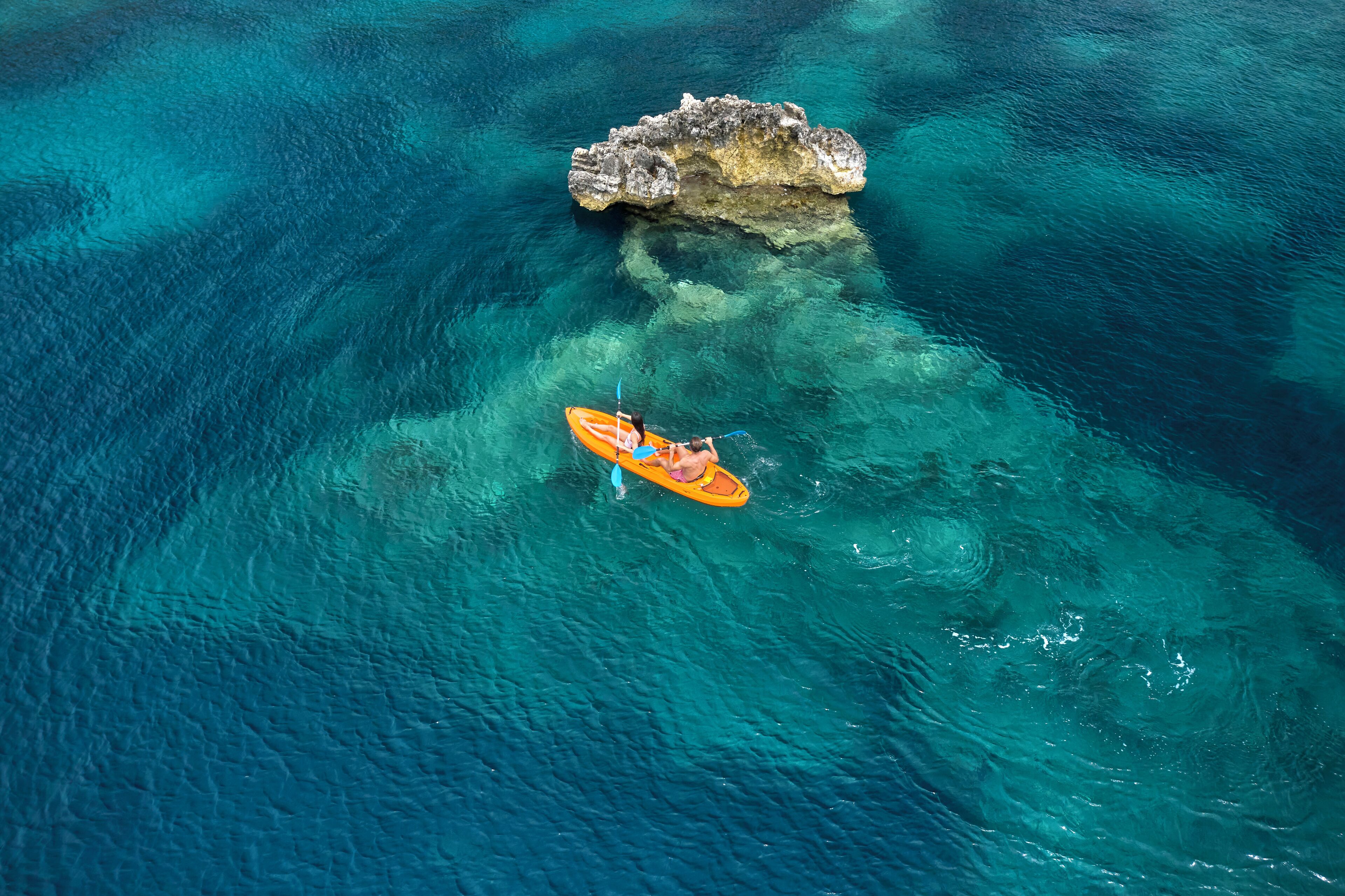 Un kayak sur une mer turquoise et limpide, avec un affleurement rocheux à proximité.