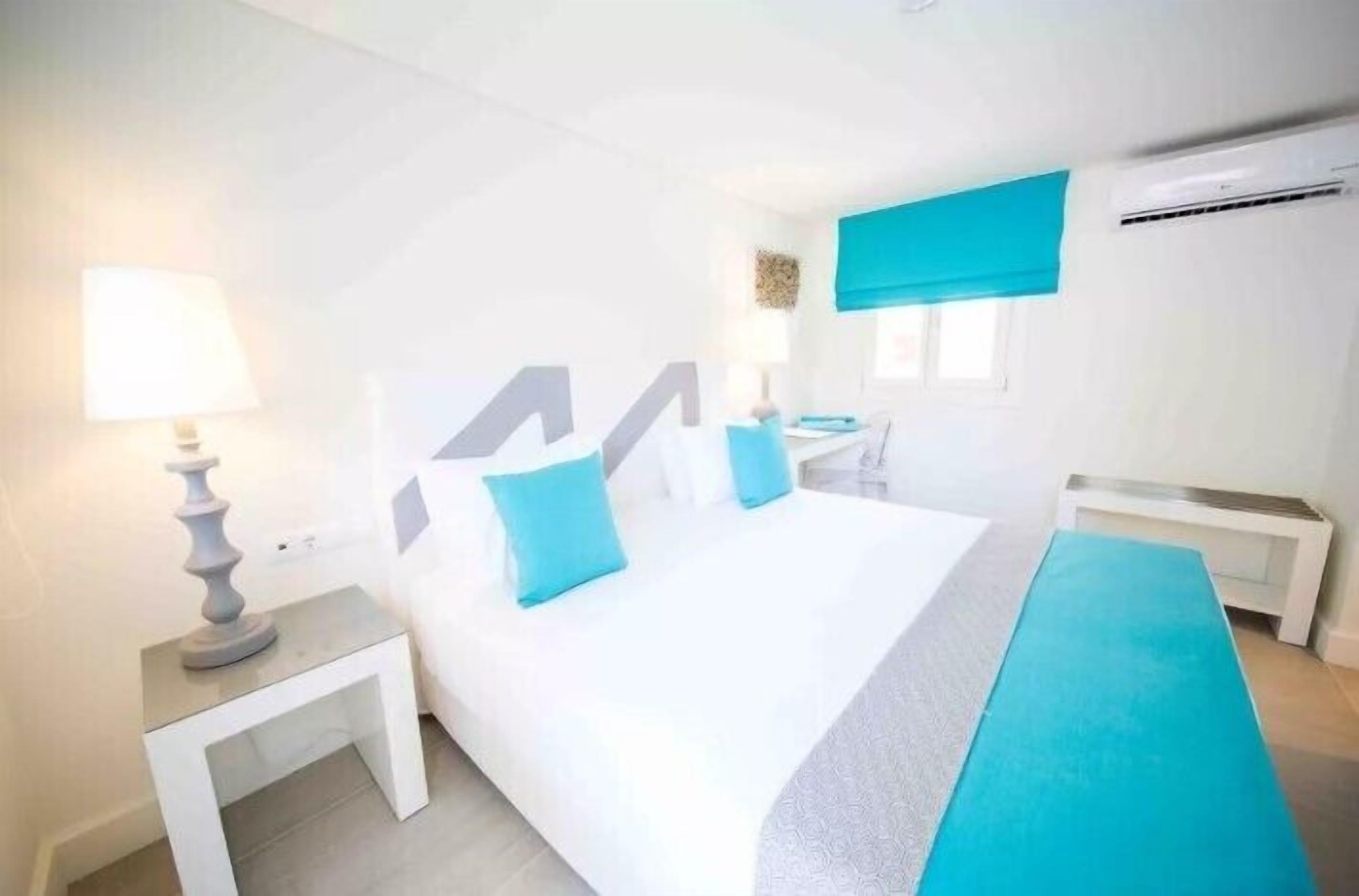 A hotel room with a large bed, a bedside table, a lamp, and a window with a blue blind.