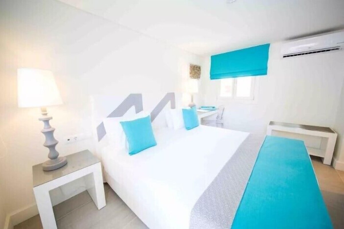 Una camera d'albergo con un letto grande, un comodino, una lampada e una finestra con una tenda blu.