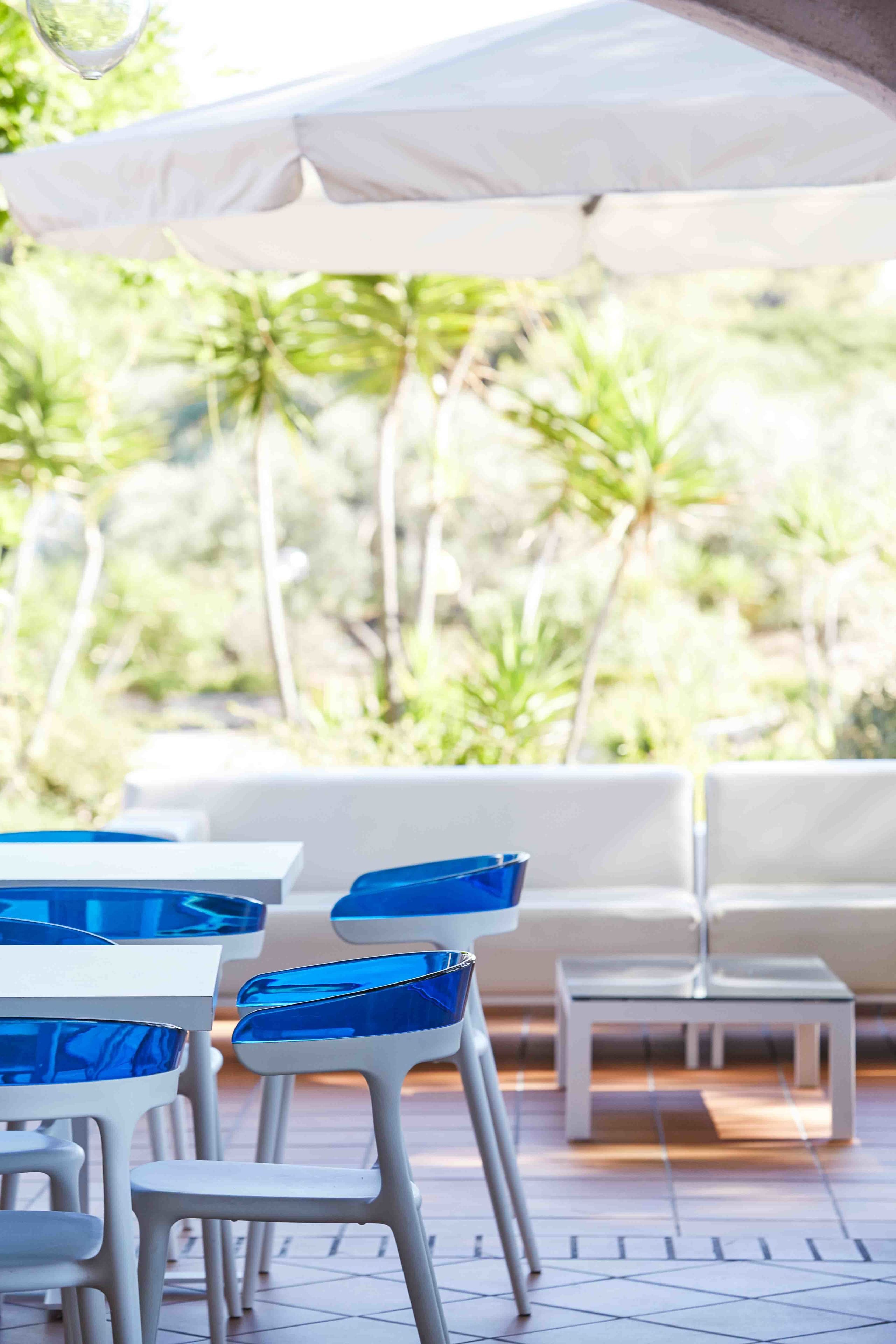 An outdoor seating area with white tables and blue chairs, surrounded by white umbrellas, and overlooking a lush green landscape.