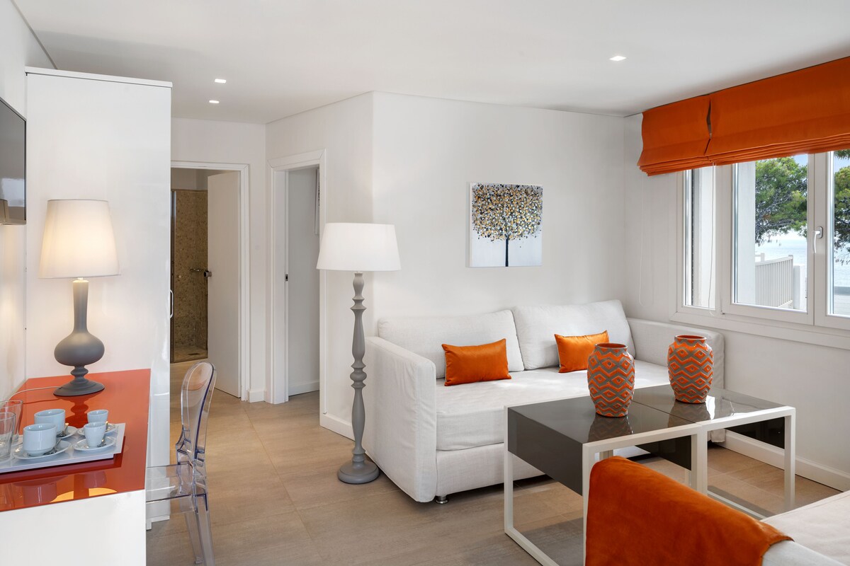 A modern living room with a white sofa, orange cushions, a glass coffee table, and a floor lamp.
