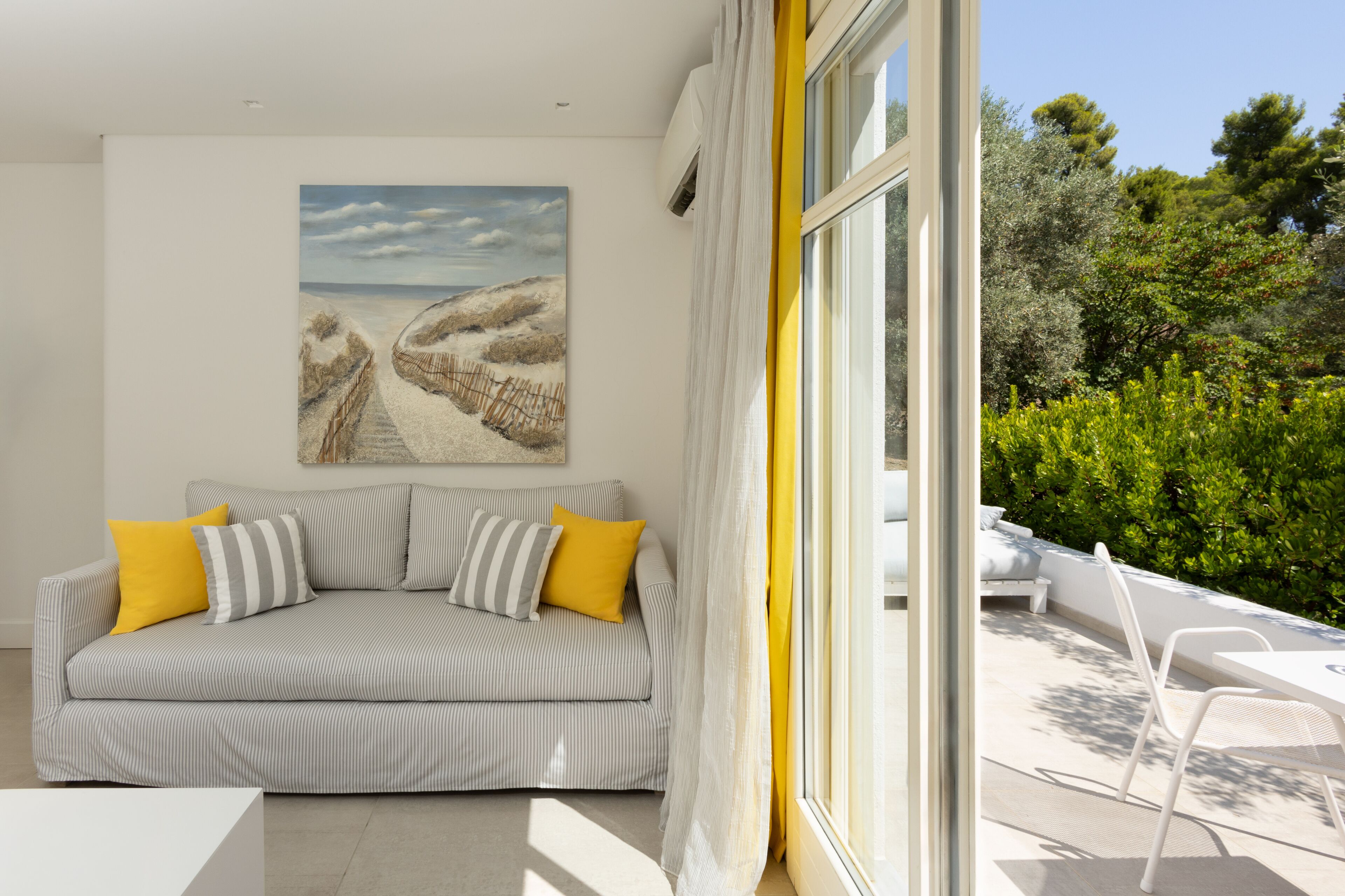 A modern living room with a striped sofa, a painting, and a view of a garden through a large window.