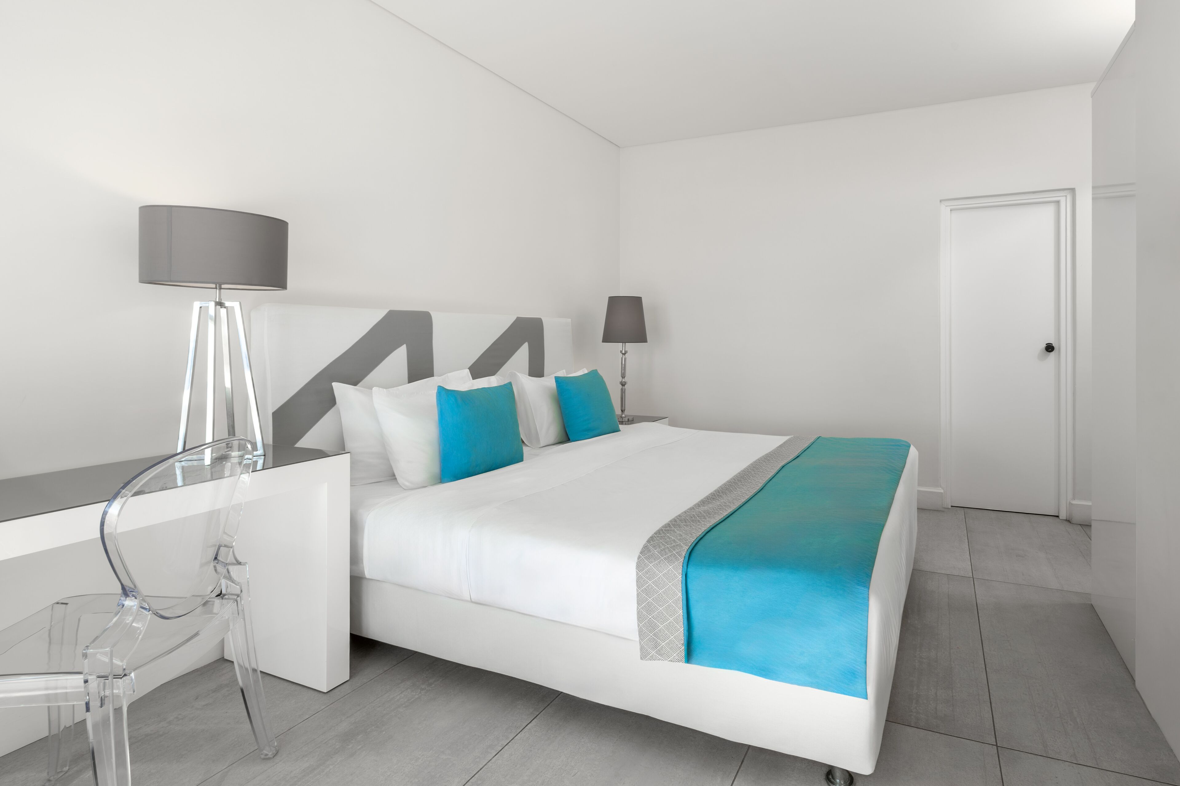 A modern hotel room with a bed, bedside tables, a desk, and a chair.