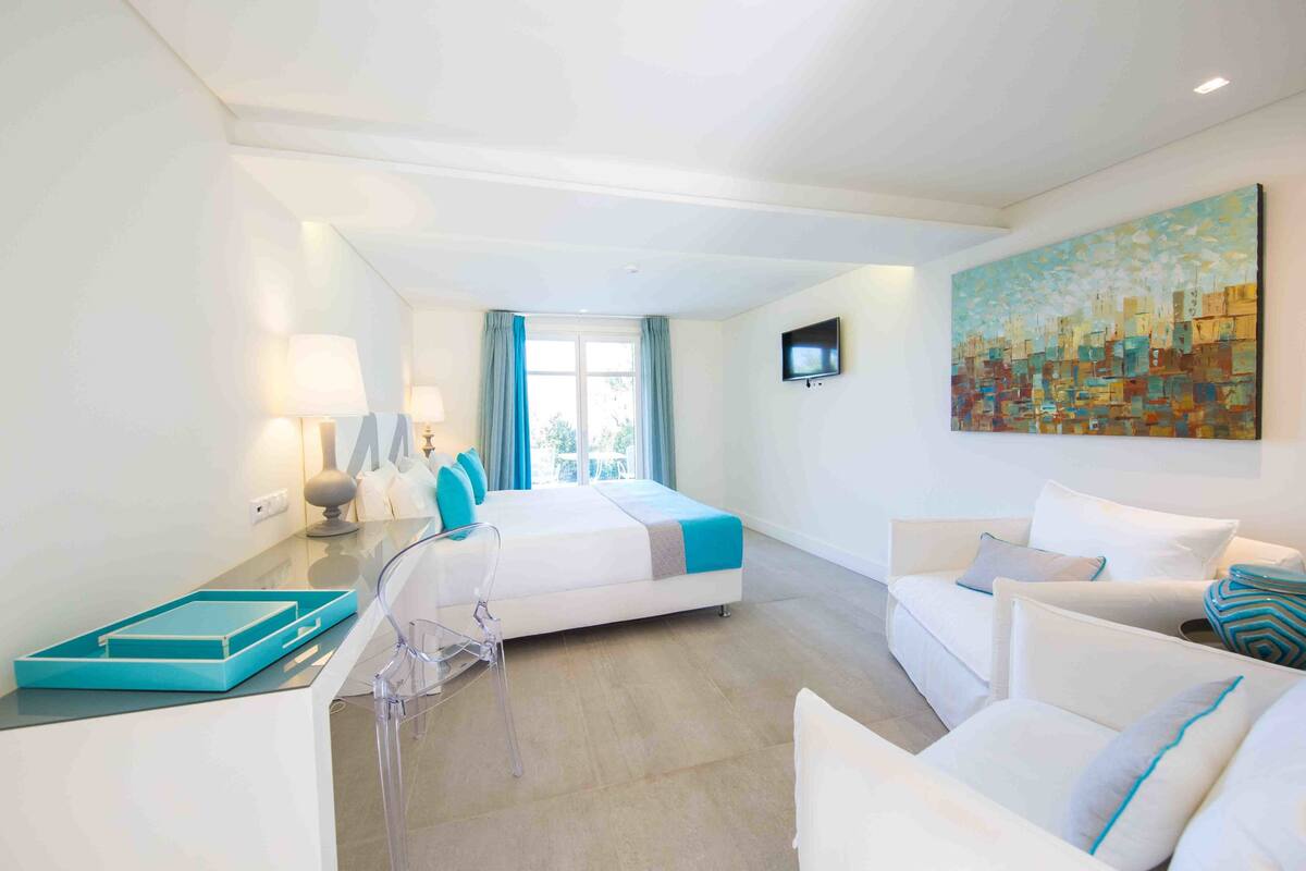 A hotel room with a bed, a sofa, a TV, and a painting on the wall.