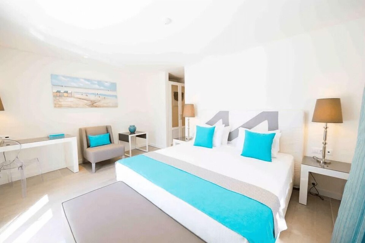Una camera d'albergo con un letto grande, una scrivania, una sedia e un quadro appeso al muro.