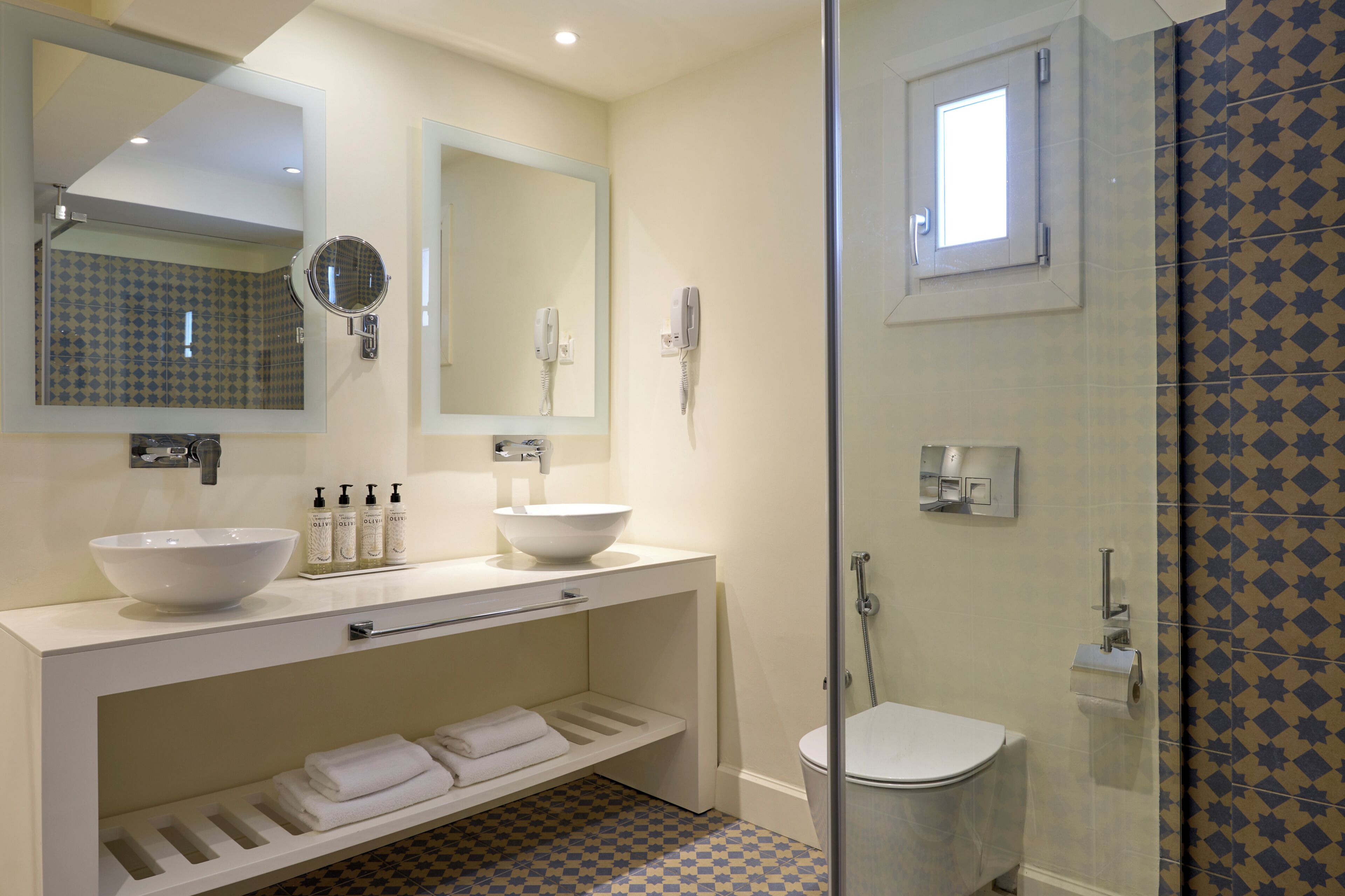 A bathroom with a white sink, a mirror, a handheld mirror, a toilet, and a shower area.