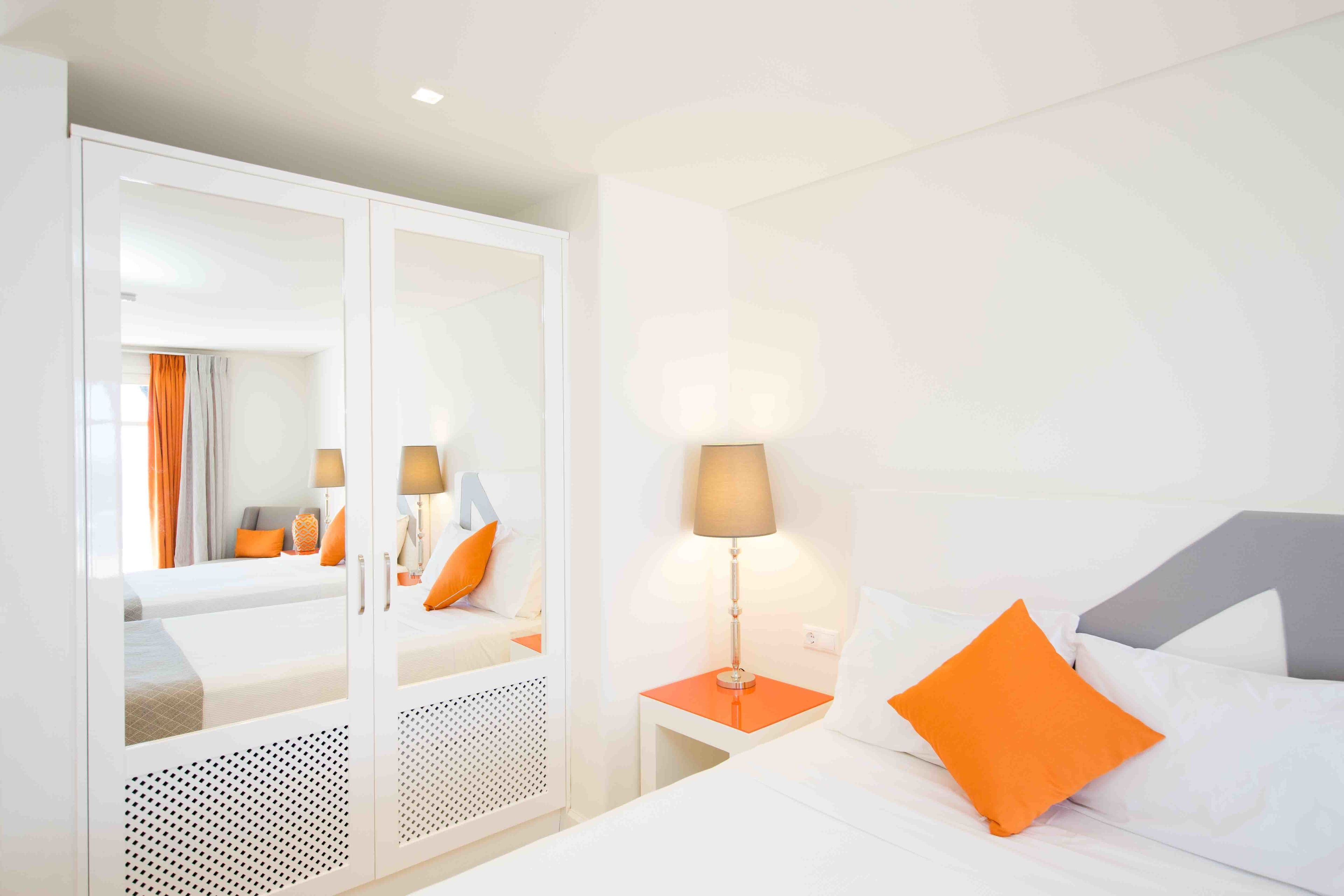 Una habitación de hotel con cama, mesita de noche y armario con espejo.