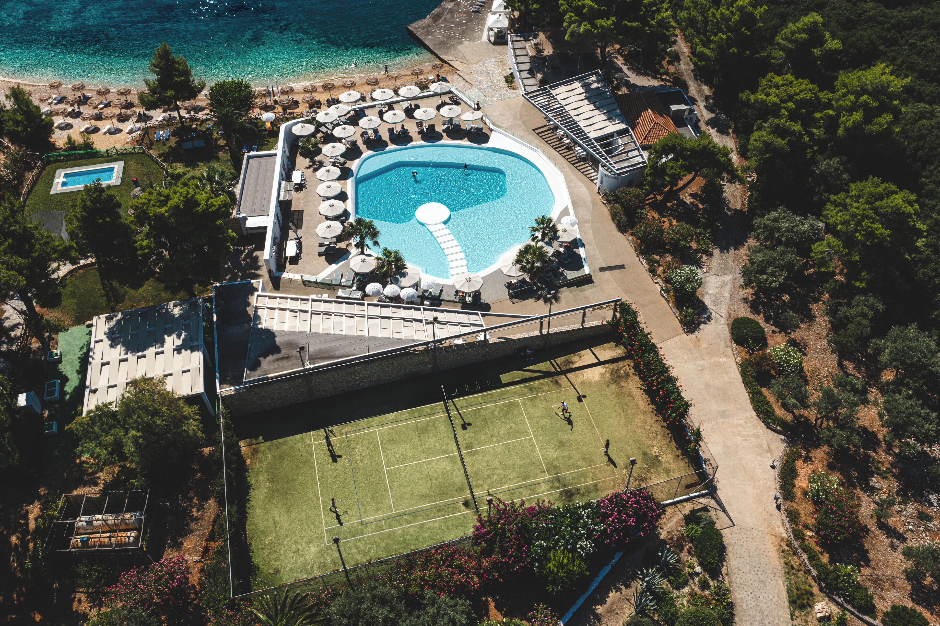 Ein Luftbild eines Resorts mit Schwimmbad, Tennisplatz und Strand.