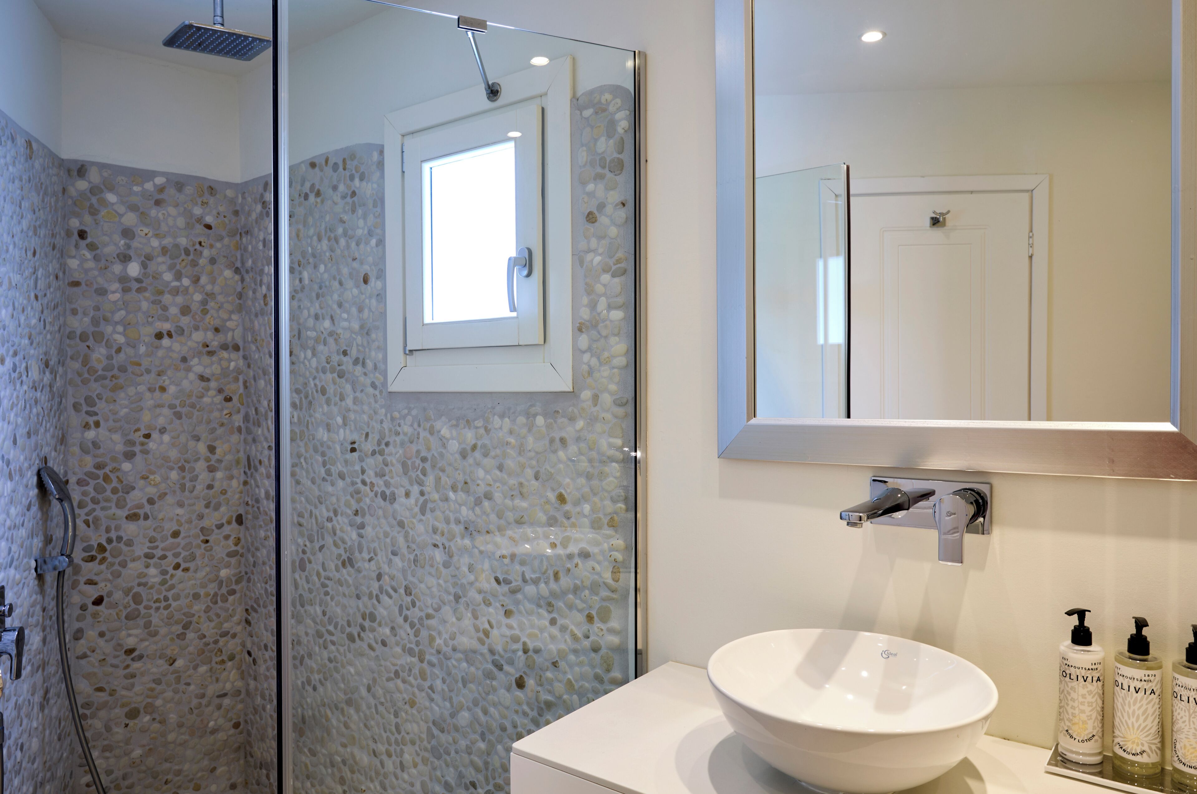 A bathroom with a glass shower enclosure, a white sink, and a mirror above the sink.