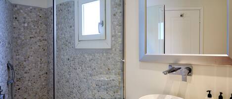 A bathroom with a glass shower enclosure, a white sink, and a mirror above the sink.