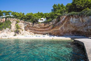 A coastal scene with a clear blue sea, a rocky cliff, and a white building on top. - Marpunta Resort (Alonissos)