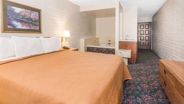 Une chambre d’hôtel avec un grand lit, une commode, un miroir et une salle de bain visible à travers une porte ouverte.