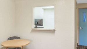Une pièce comprenant une table ronde, une chaise, une petite fenêtre avec un écran d’ordinateur et une porte.