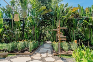 A garden pathway with directional signs, surrounded by lush greenery and flowering plants. - Hotel Komune and Beach Club Bali (Keramas)
