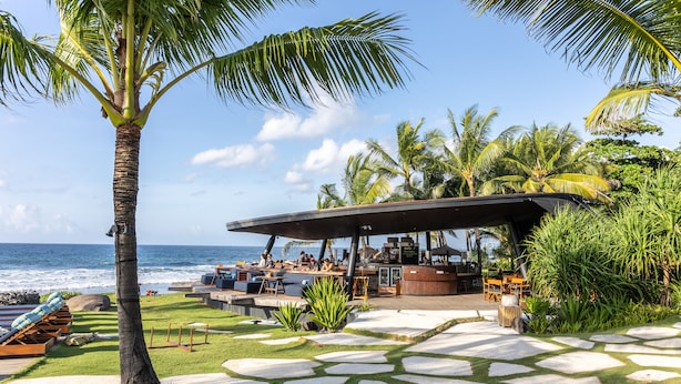 A beachside resort with a bar area, outdoor seating, and a view of the ocean.