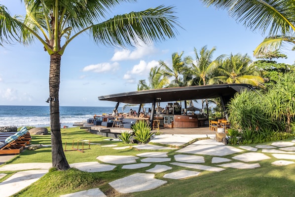 A beachside resort with a bar area, outdoor seating, and a view of the ocean.