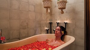 A bathtub filled with rose petals and flowers, with a wall-mounted plant and candles.