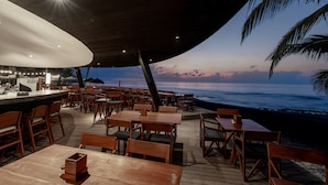 A wooden deck with tables and chairs overlooking the ocean at sunset.