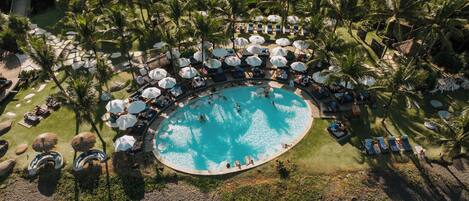 An aerial view of a resort with a central swimming pool surrounded by lounge areas and palm trees.