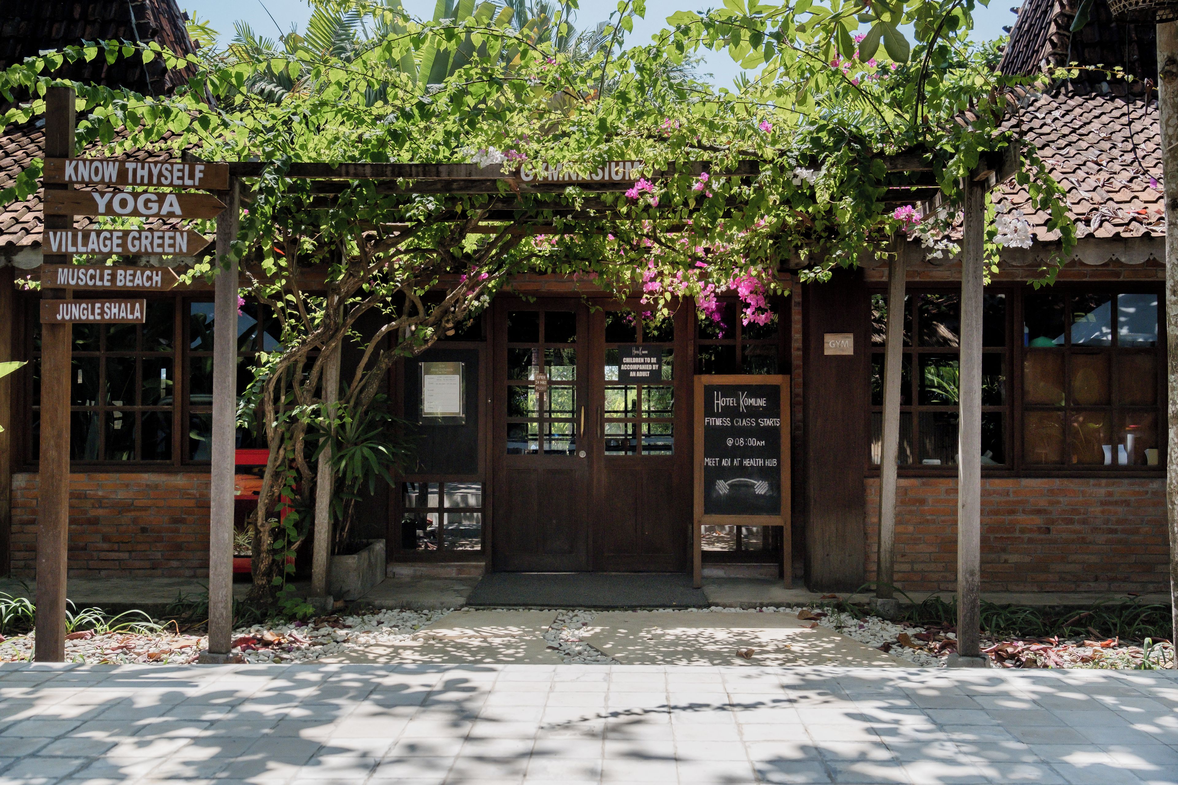 A building with a wooden entrance, signs for yoga, village green, muscle beach, and jungle shala.
