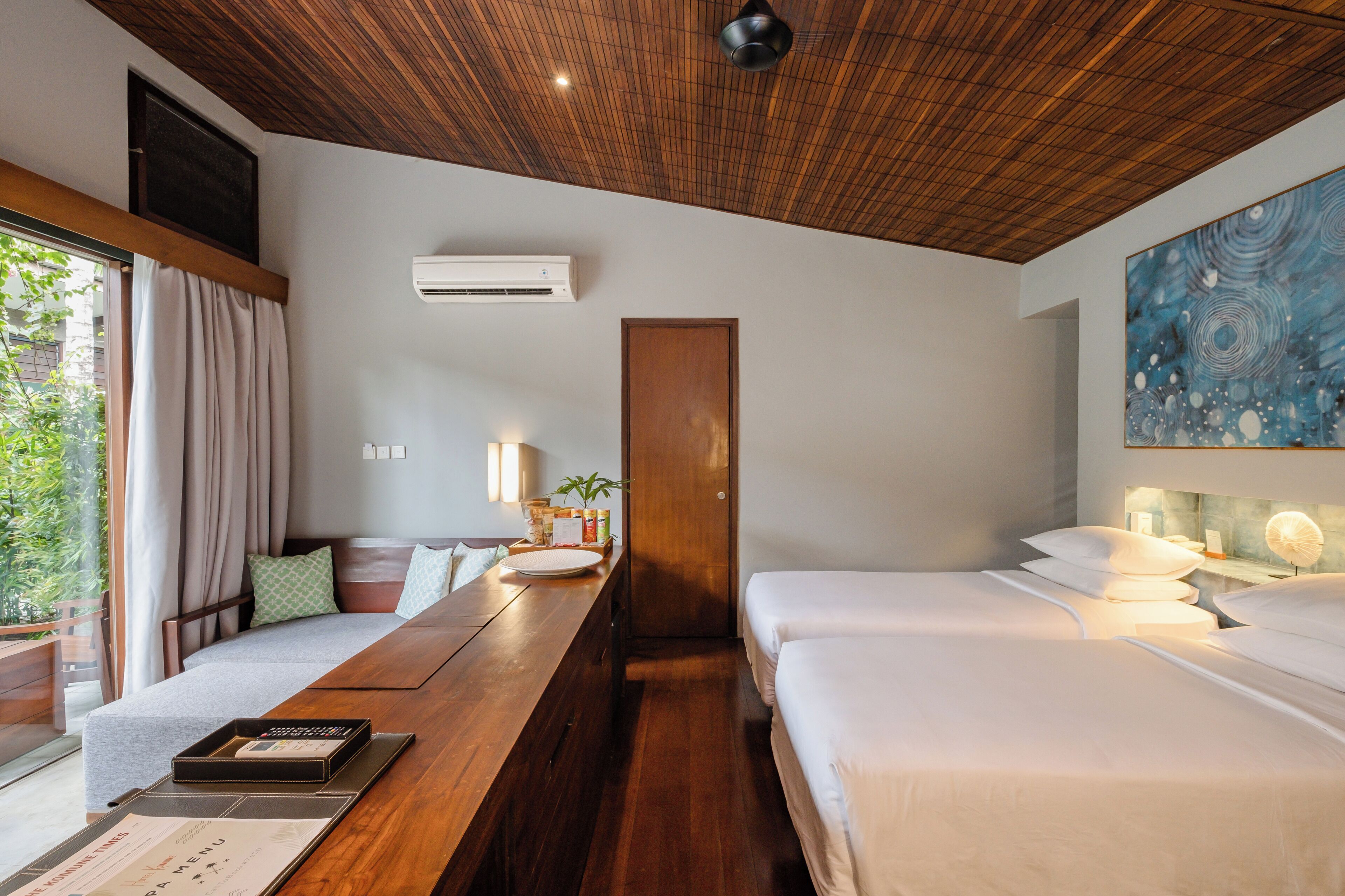 Een hotelkamer met een houten plafond, een bed, een bureau met een menukaart en een schilderij aan de muur.
