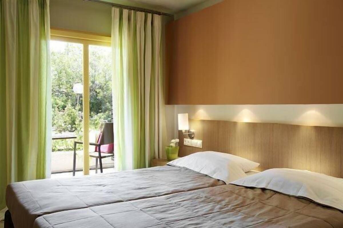 A hotel room with a bed, a chair, and a table by a window with curtains.