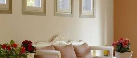 A modern living room with a beige sofa, three windows, and two side tables with potted plants.