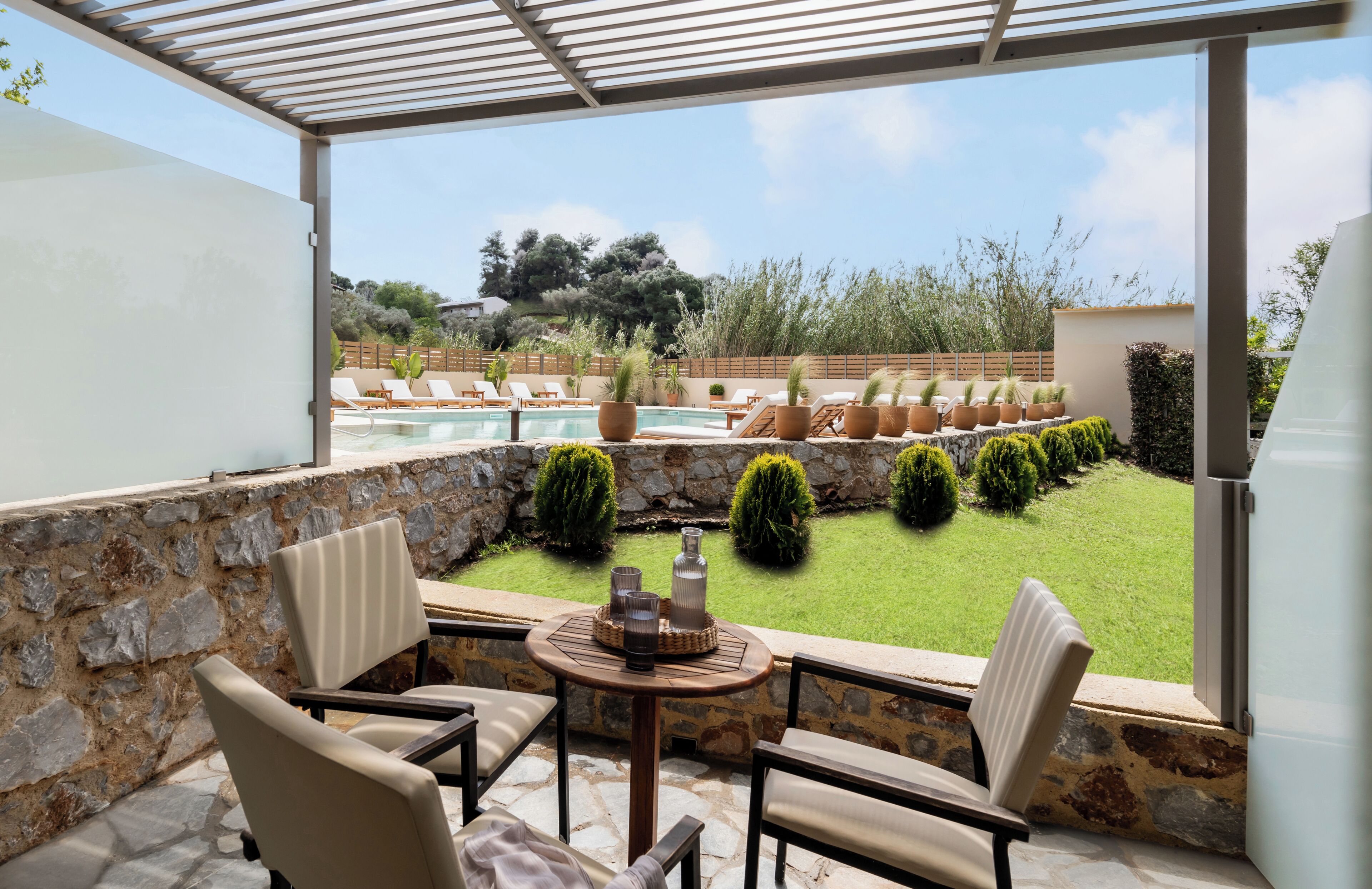 A covered outdoor seating area with a stone wall, a pool, and a view of the garden.
