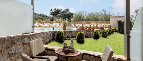 A covered outdoor seating area with a stone wall, a pool, and a view of the garden.