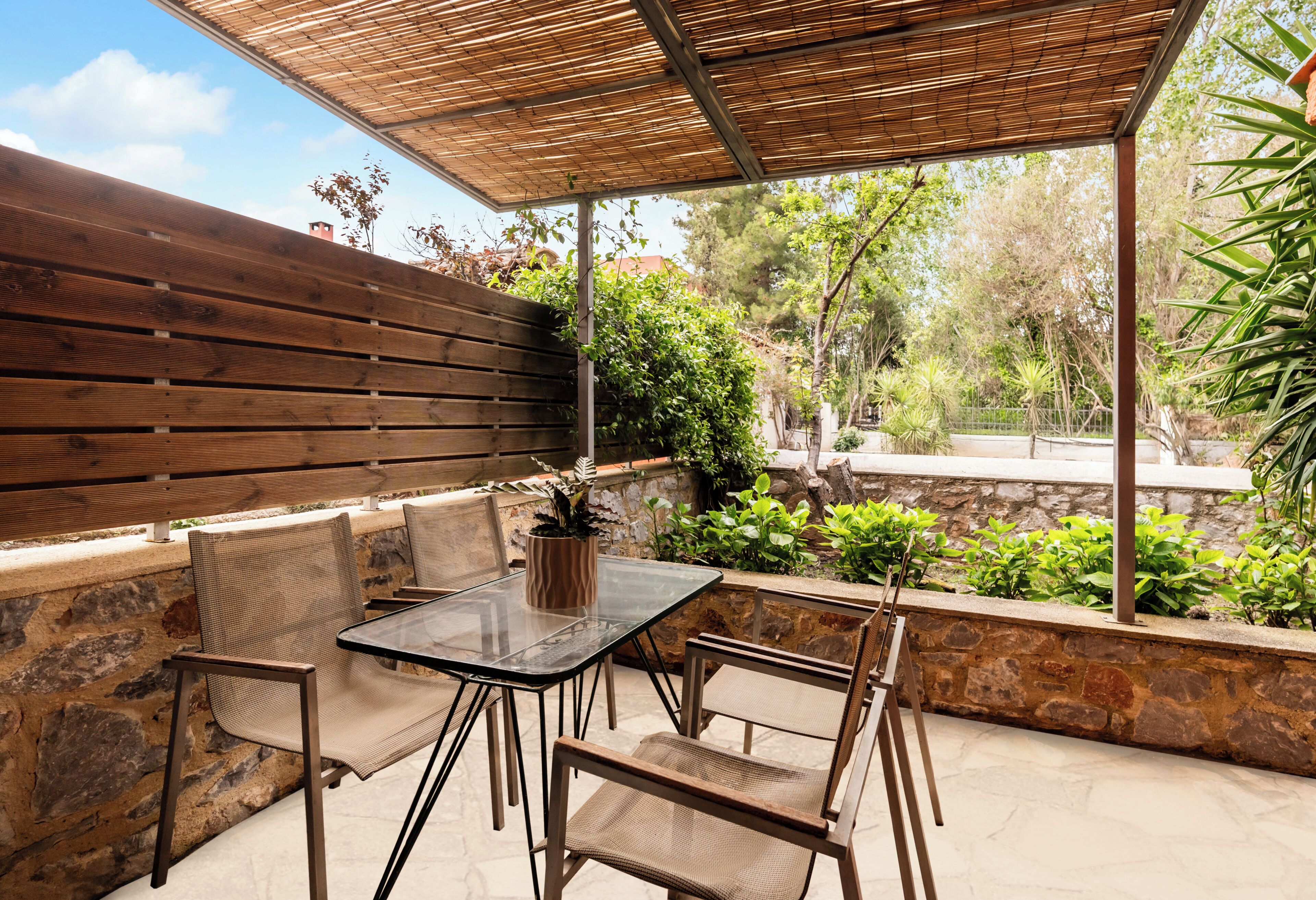 Une terrasse extérieure avec une table et des chaises, un mur en bois et une vue sur la verdure.