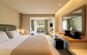 A hotel room with a large bed, a desk with a coffee maker, a TV, and a view of the outdoor patio. - Astoria Hotel (Skiathos)