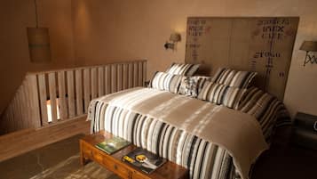 Ein Schlafzimmer mit einem großen Bett, gestreifter Bettwäsche, einer hölzernen Sitzbank mit Büchern, einer Pendelleuchte und einer Wand mit einem Vintage-Schild.