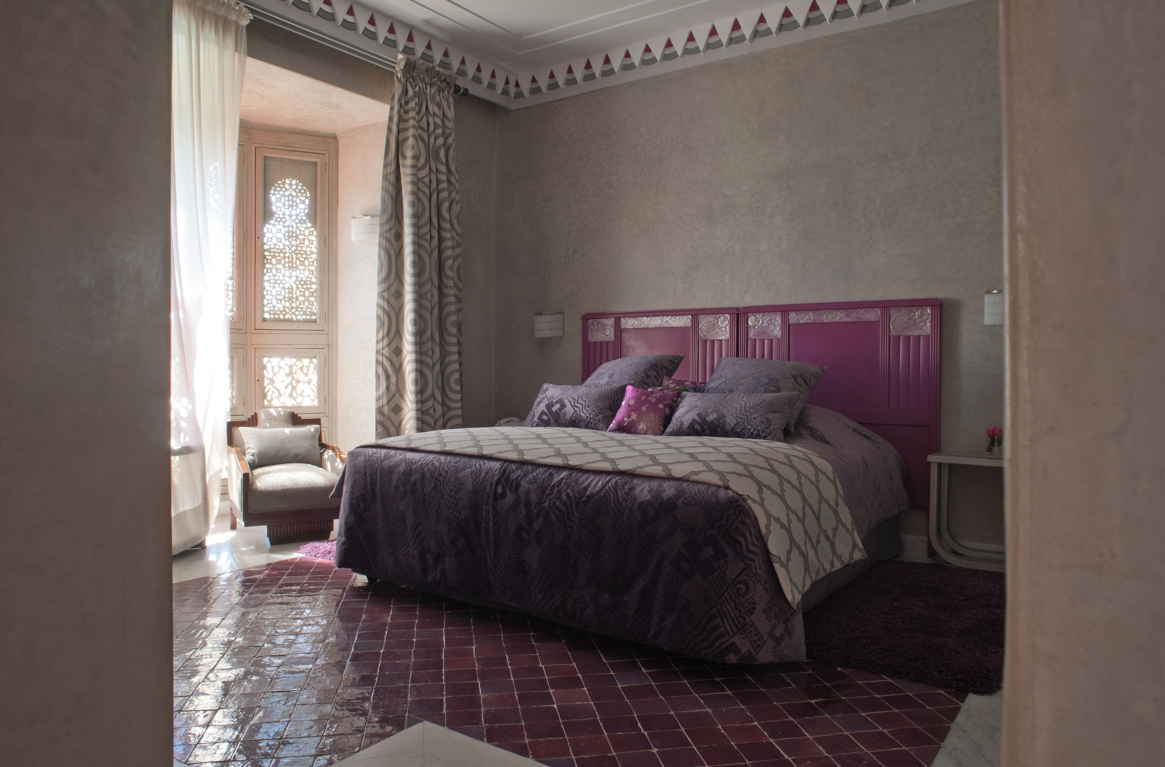 A bedroom with a bed, a chair, a nightstand, and a window with curtains.