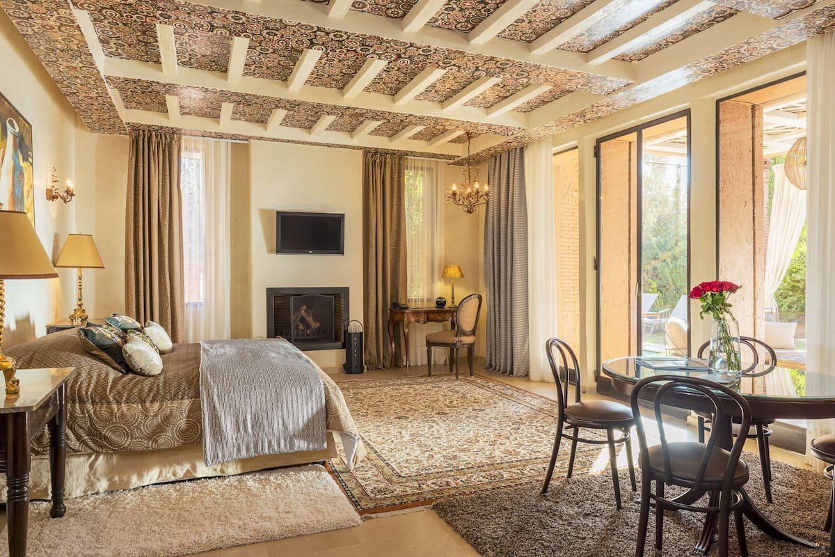 Une chambre à coucher comprenant un lit, un bureau, une chaise, une cheminée et une grande fenêtre.