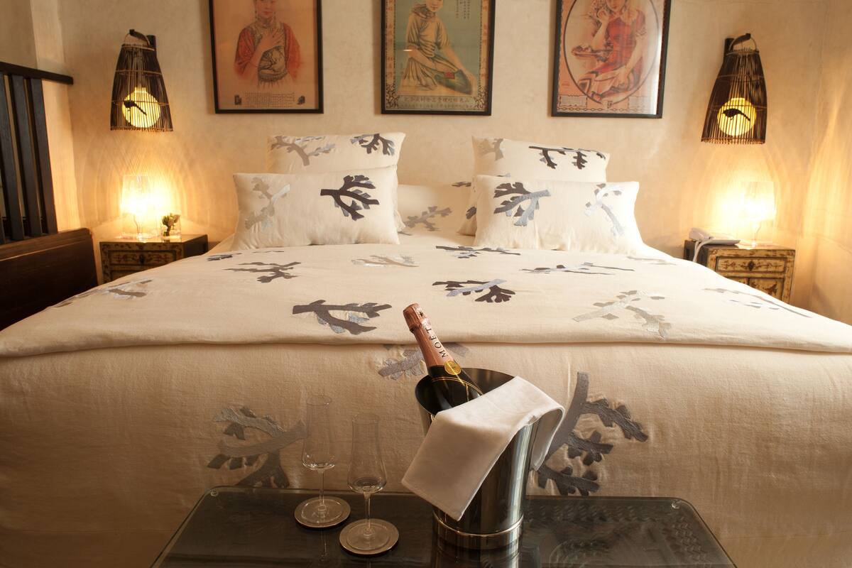Une chambre d’hôtel avec un lit, deux tables de chevet, une bouteille de champagne et deux verres.